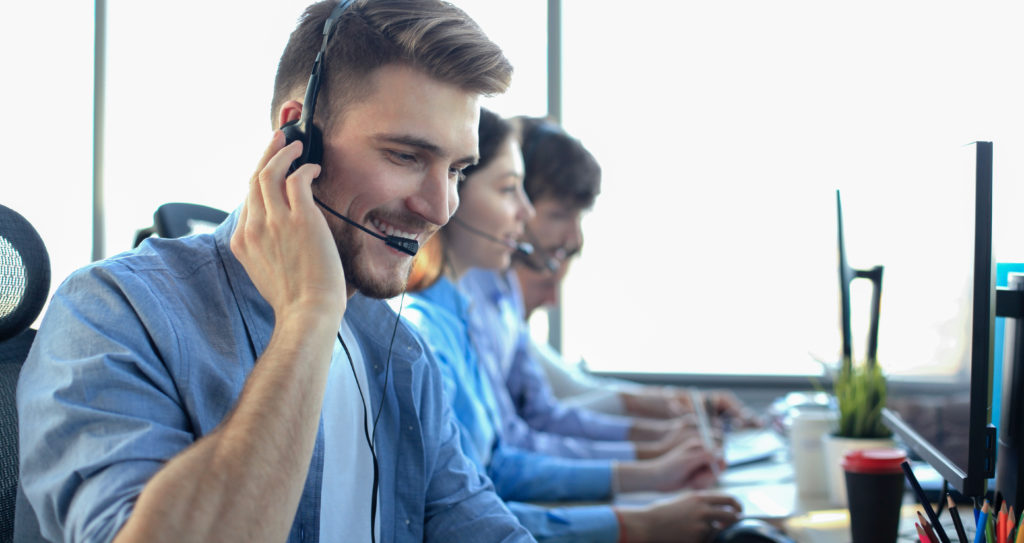 Portrait of call center worker accompanied by his team. Smiling customer support operator at work.